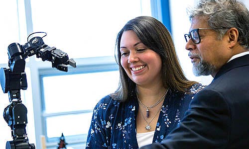A student and faculty member looking at a robotic arm in a lab room