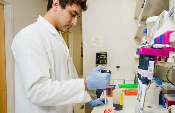 A career training participant in medical lab coat pouring liquid into vials.