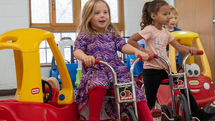 Three children riding on tricycles and Little Tikes cars.