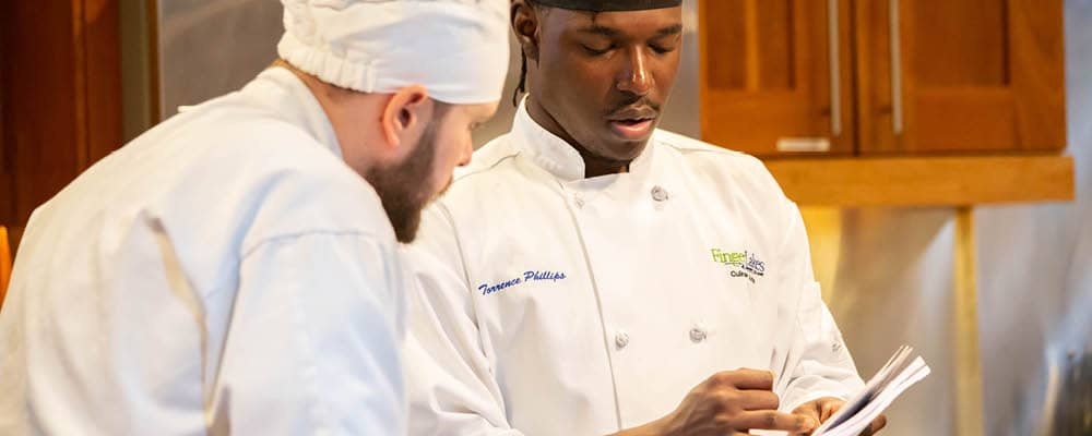 Two culinary students reviewing information in a kitchen.