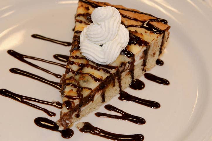A slice of pie drizzled with chocolate and topped with a whipped cream.