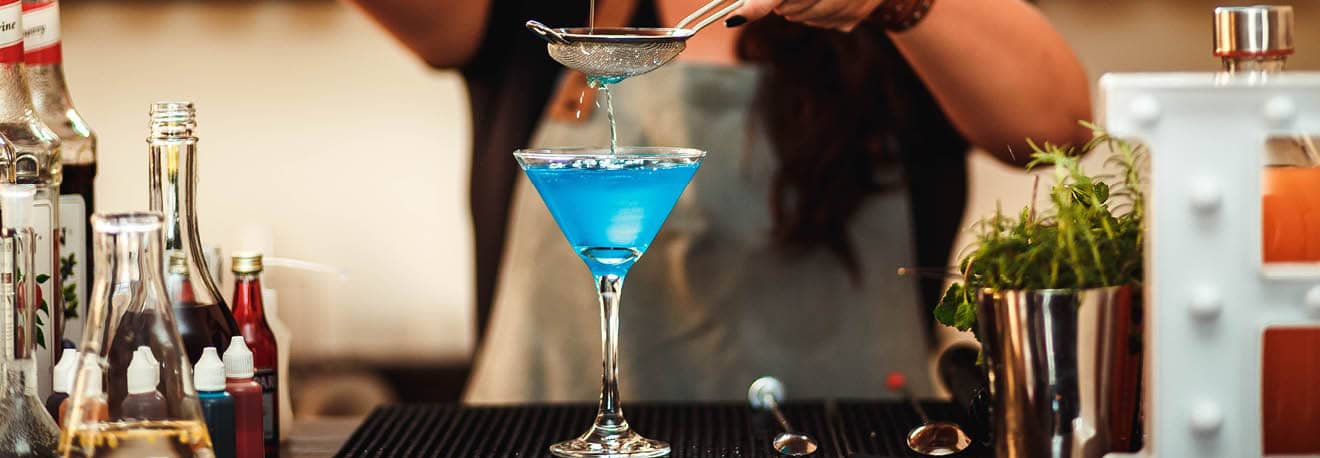 A bright blue cocktail poured into a tall martini glass.
