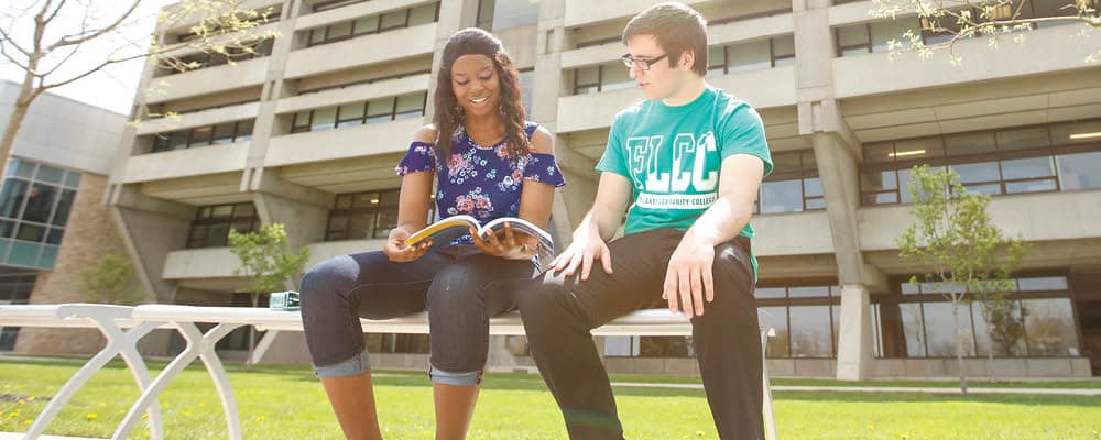 Two students study a text together while sitting on a bench outside of Finger Lakes Community College.
