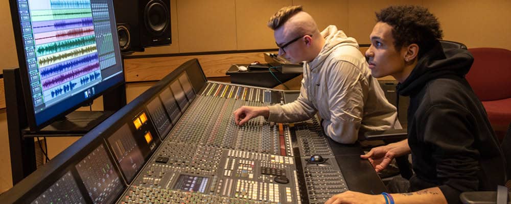 Two music recording technology students adjusting setting on a professional studio soundbound.