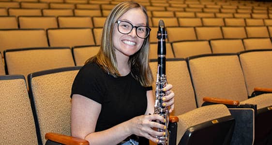 Band member holding a clarinet while sitting in a performance hall.