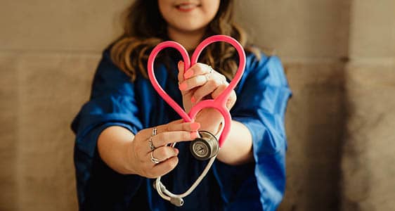 A medical professional holding a stethoscope in the shape of a heart.
